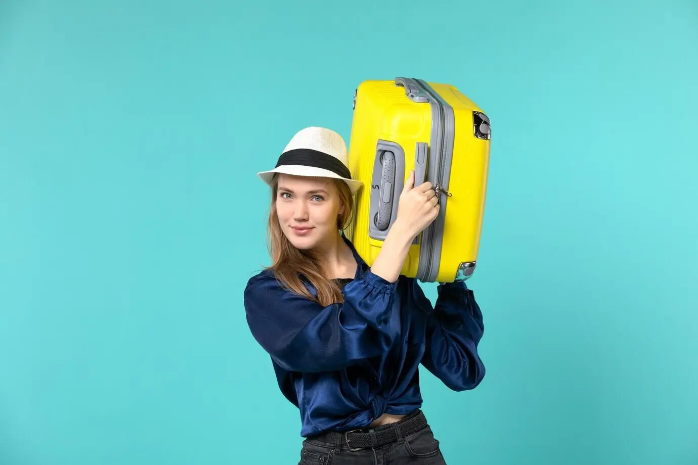 Vorderansicht einer jungen Frau, die in den Urlaub reist und eine große Tasche hält, vor hellblauem Hintergrund; Reisen, Meer, Reise, Urlaub, Fahrt.